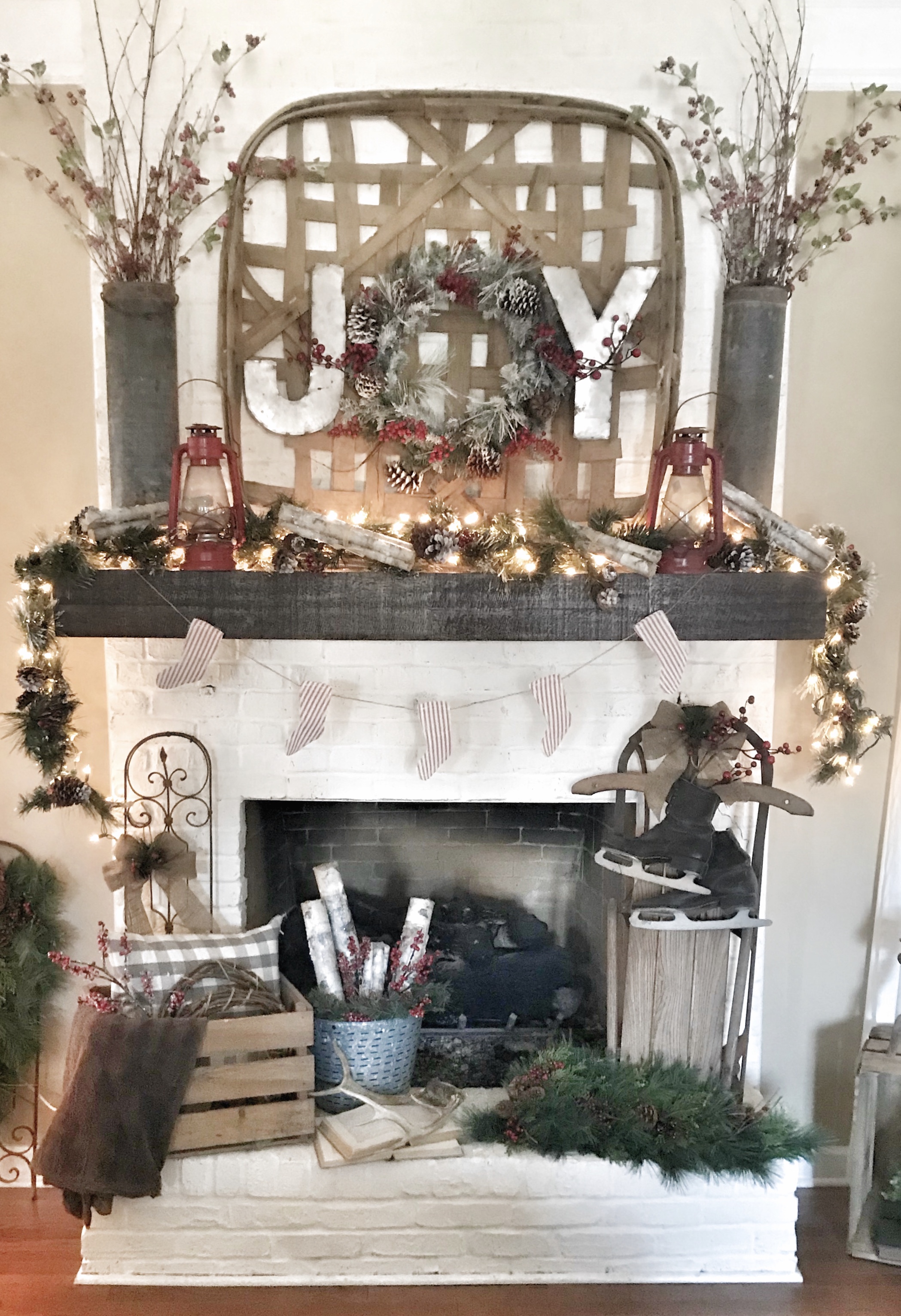 mantel decorated for Christmas with garland, lights, and joy sign